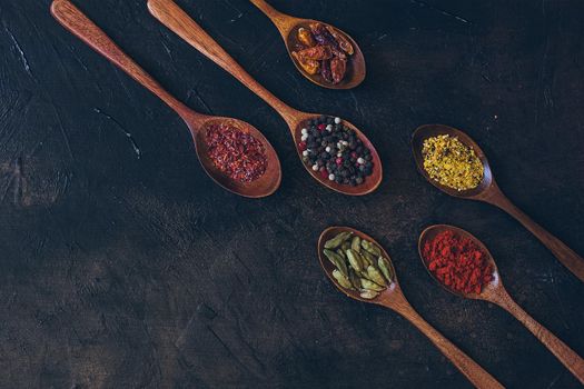 Various spices in wooden spoons on old black table