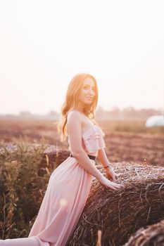 Beautiful romantic model girl outdoors dressed in tender long dress in the field in sunset light. Wind blowing long hair. Glow Sun, Sunshine. Backlit. Toned in warm colors.