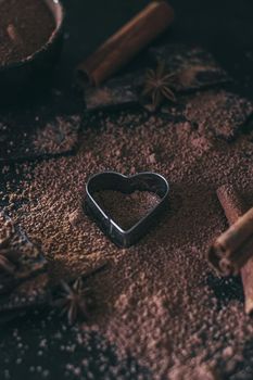 Chocolate bar pieces with cocoa powder and heart shape on dark background, cope space.