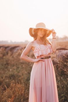 Beautiful romantic model girl outdoors dressed in tender long dress in the field in sunset light. Wind blowing long hair. Glow Sun, Sunshine. Backlit. Toned in warm colors.