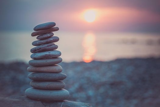 Stones pyramid on sand symbolizing zen, harmony, balance. Ocean at sunset in the background.