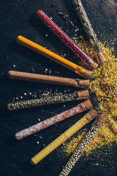 A set of spices in small jars with cork lids. Pink salt, ginger, turmeric, masala, paprika, smoked paprika. Spices on a black surface