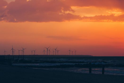 Wind turbine power generators silhouettes at ocean coastline at sunset. Alternative renewable energy production