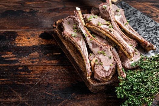 Grilled mutton Chops steaks on butcher board with meat cleaver. Dark wooden background. Top view. Copy space.