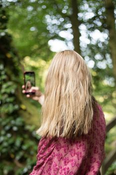 Woman taking pictures with smartphone in the forest.