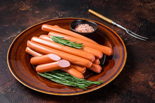 Wiener raw sausages in a rustic plate with herbs. Dark background. Top view.