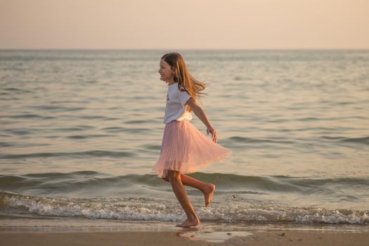 Happy little girl is spinning and dancing on the beach on a Sunny day