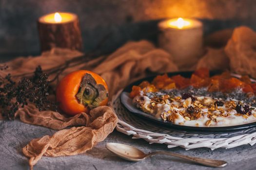 Healthy breakfast concept. Oatmeal granola with yogurt, dried fruit, seeds, honey, persimmon in bowl over grey concrete background. Allergy-friendly, gluten free concept.