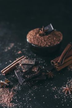 Chocolate bar pieces with cocoa powder on dark background, cope space.