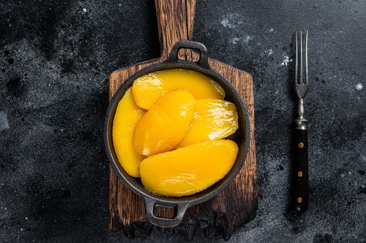 Canned mango slices in bowl. Black background. Top view.