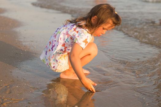 The little cute girl sitting and playing on the beach.