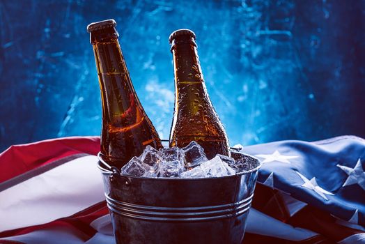 two bottles of beer in an ice bucket with the American flag lying nearby. Independence Day celebration concept