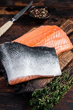 Salmon fillet fish on a wooden board with herbs and salt. Dark wooden background. Top view.