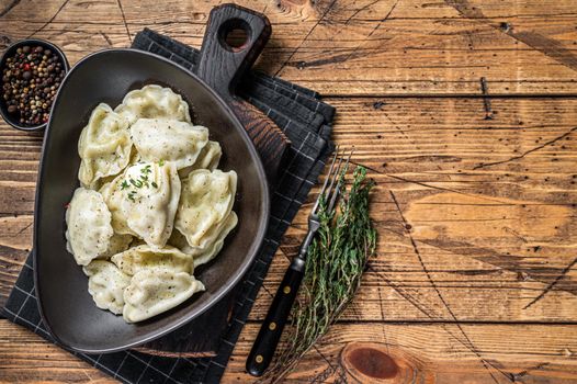 Dumplings pierogi with potato in a plate with herbs and butter. Wooden background. Top View. Copy space.