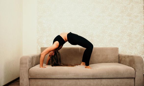 Young woman with long hair, fitness instructor in black sportswear, doing stretching and pilates on yoga mat at home. Female fitness yoga routine concept. Healthy lifestyle harmony and meditation