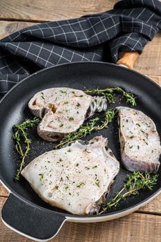 Fresh raw wolffish fillet steaks in a pan with herbs. wooden background. Top view.