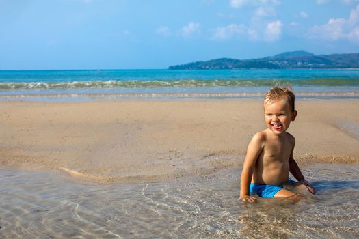 Joyful adorable small boy enjoying water while resting and sitting in water on coastline in summertime