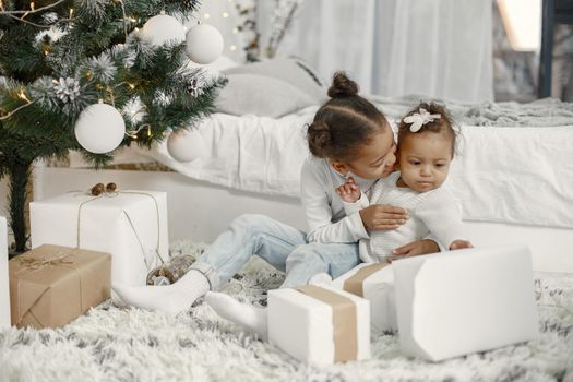 Child in a white sweater. Daughters stitting near Christmas tree.Two sisters at home.