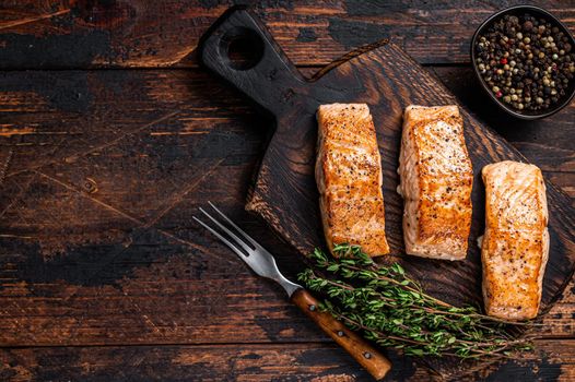 Fried Salmon Fillet Steaks on a wooden board with thyme. Dark wooden background. Top view. Copy space.