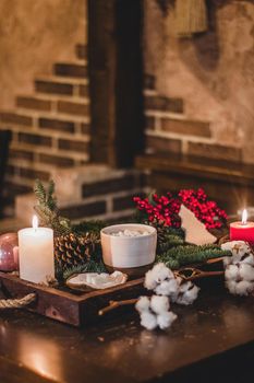 Christmas hot chocolate with mini marshmellows in an old ceramic mug with candles on a wooden background.