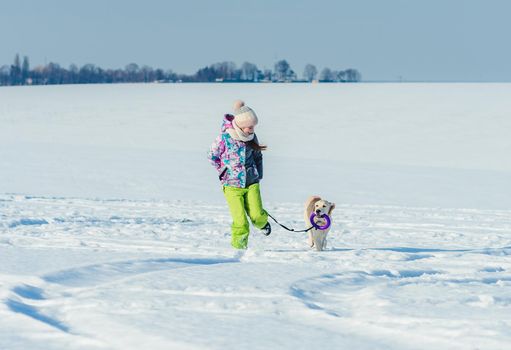 Happy girl running with cute dog in sparkling snow