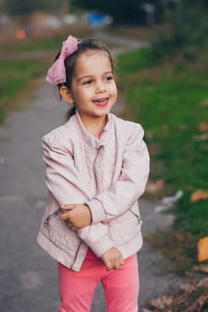 Young smiling girl in a pink jacket and pink leggings in the park