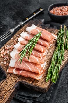 Prosciutto crudo parma ham, dry cured pork meat on a wooden board. Black background. Top View.