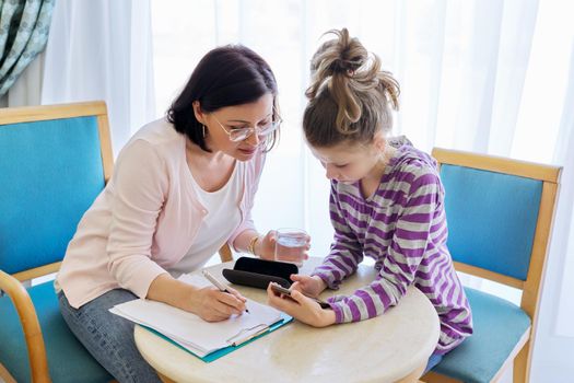 Preteen child girl at meeting with therapist, social worker, counselor in office, kid showing his smartphone to teacher. Psychology, education, therapy, mental health, children concept