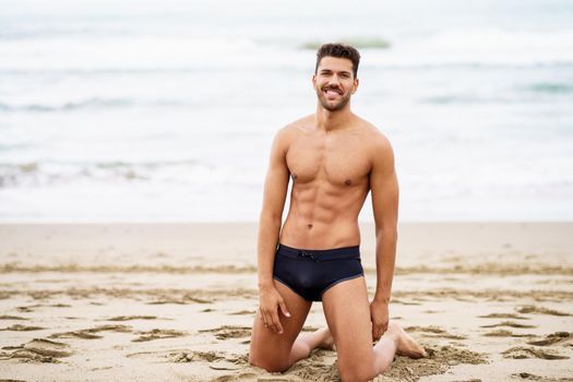 Handsome muscular man on his knees on the sand of the beach