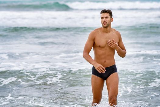 Handsome muscular man bathing on the beach wearing swimwear