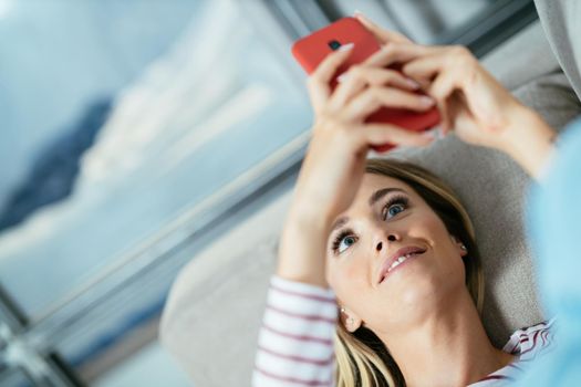 Close-up of woman using her smartphone lying on the sofa at home.