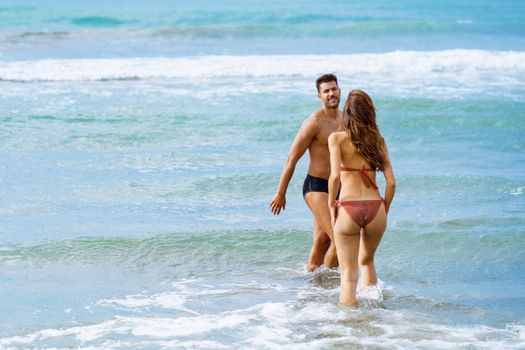 Young couple of beautiful athletic bodies bathing together on the beach enjoying their holiday at sea