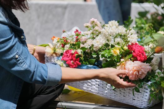 Female florist doing floral arrangement outdoors. Flower basket creation workflow.