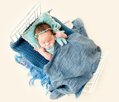 cute newborn baby girl with nipple sleeping in a little bed