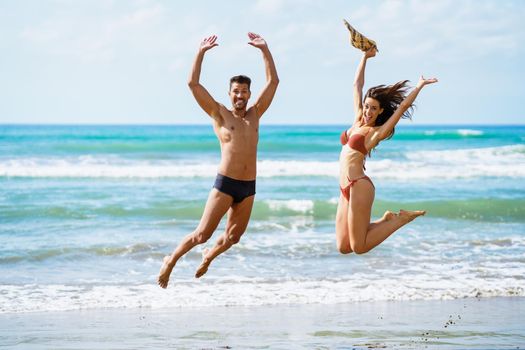 Funny young couple with beautiful bodies in swimwear jumping on a tropical beach.