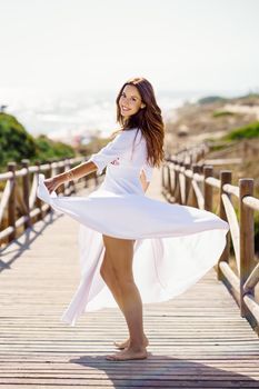 Young pretty woman moving a beautiful white dress in Spanish fashion on a boardwalk on the beach.