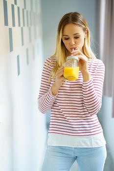 Young caucasian woman drinking a glass of natural orange juice at home.