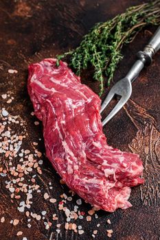 Raw machete skirt beef steak on meat fork. Dark background. Top view.