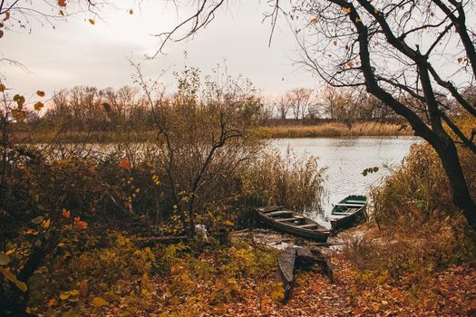 A boat near the river shore filled with water and golden autumn leavesin sunset time.