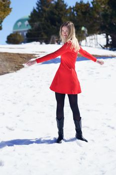 Young blonde woman wearing a red dress and black stockings opening her arms in happiness in the snowy mountains, in Sierra Nevada, Granada, Spain.