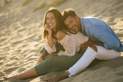 Happy loving couple laughing together sitting on the sand of the beach