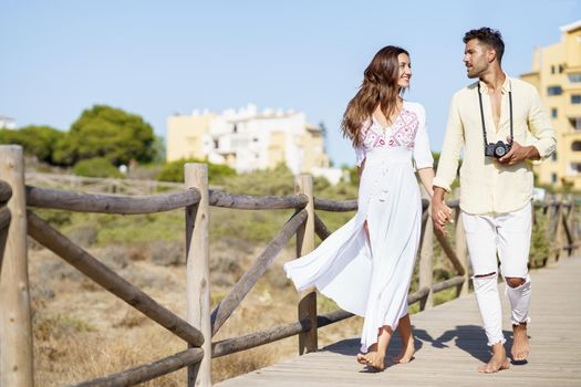 Happy loving couple walking along a wooden path towards the beach in a coastal area.