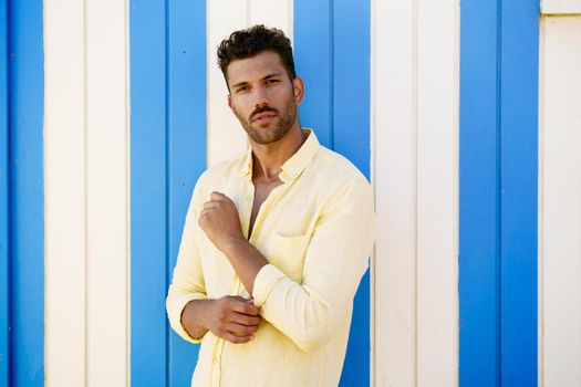 Young man, fashion model, posing in front of a beach booth looking at the camera.