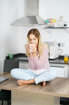 Young caucasian woman smelling a cup of coffee at home.