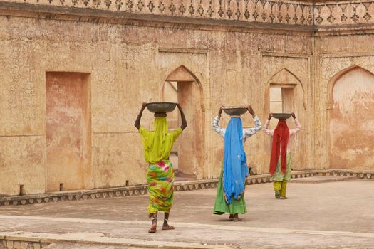 JAIPUR, RAJASTHAN, INDIA - JULY 30, 2008: Female laborers transporting water and plaster in bowls carried on the head during the restoration of a palace inside Amber Fort in Jaipur, Rajasthan, India.