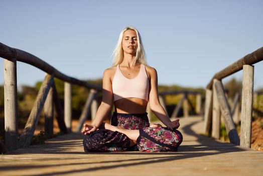 Woman enjoying the sunset on a beautiful beach in Cadiz, Andalusia, Spain. Caucasian female practicing yoga on wooden bridge.