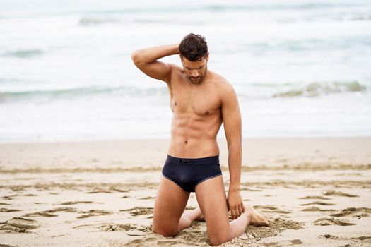 Handsome muscular man on his knees on the sand of the beach