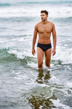 Handsome muscular man bathing on the beach wearing swimwear