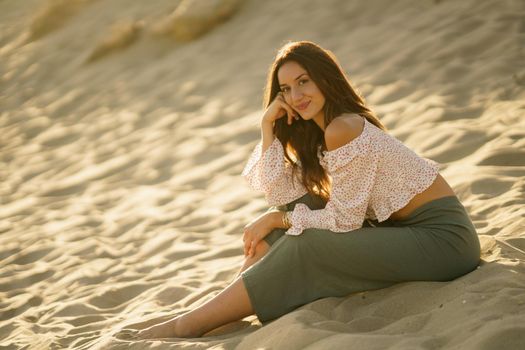 Attractive woman sitting on the sand of the beach looking at the horizon.