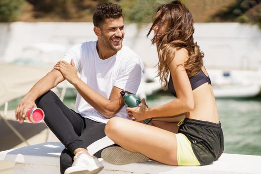 Young sporting couple hydrate themselves with water in metal bottles while taking a break after sport.